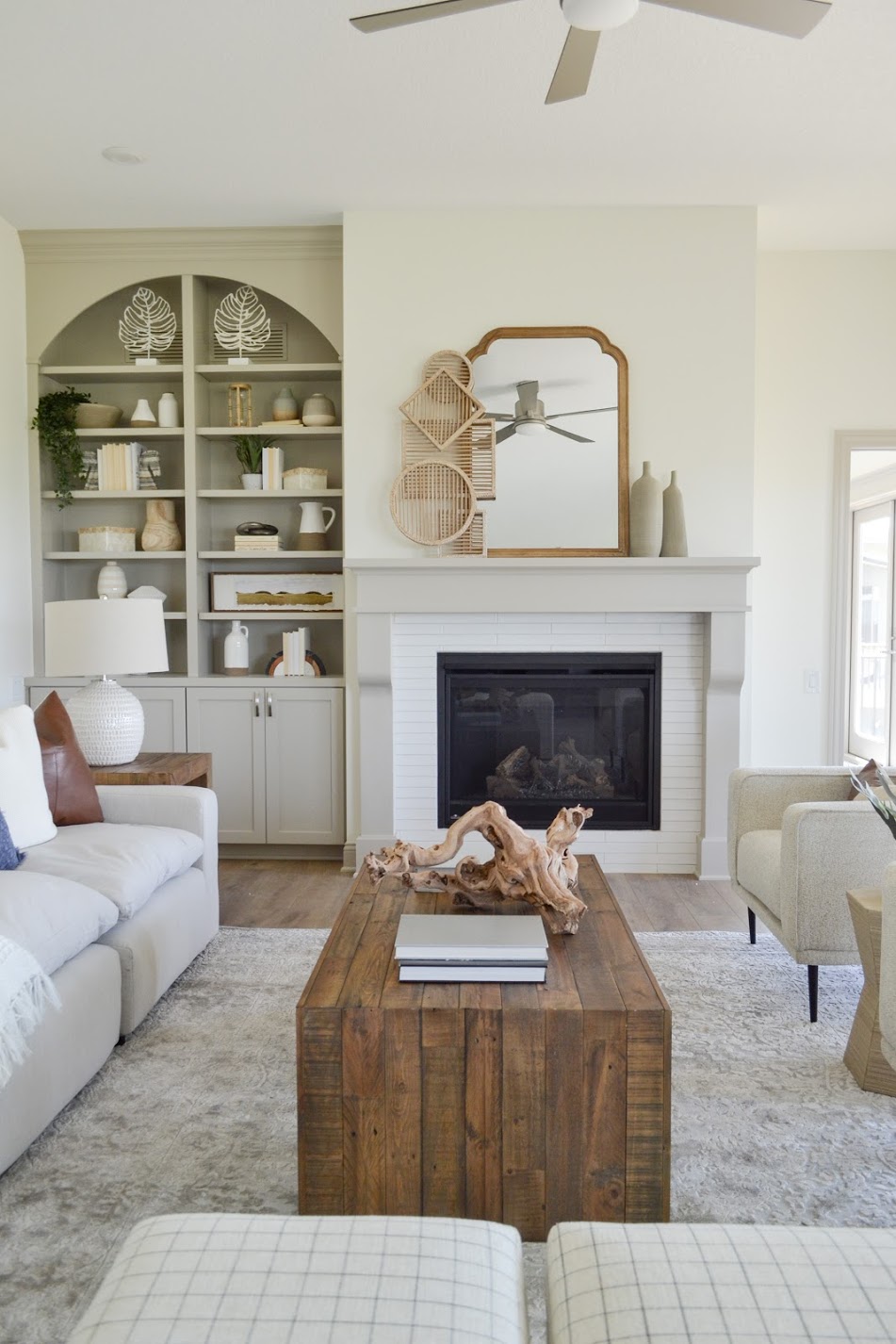 Modern Organic European Farmhouse living room with mirror above fireplace. Built-in taupe shelves and cabinets styled with vases, plants,  and books. 
