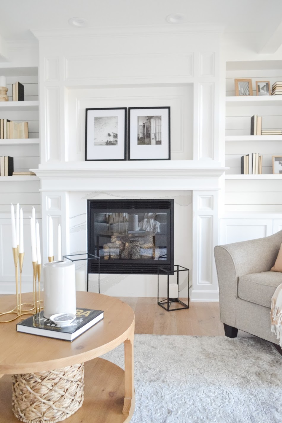 Coastal white living room with marble fireplace façade and millwork trim with shiplap shelving. Black and white framed prints and décor. 