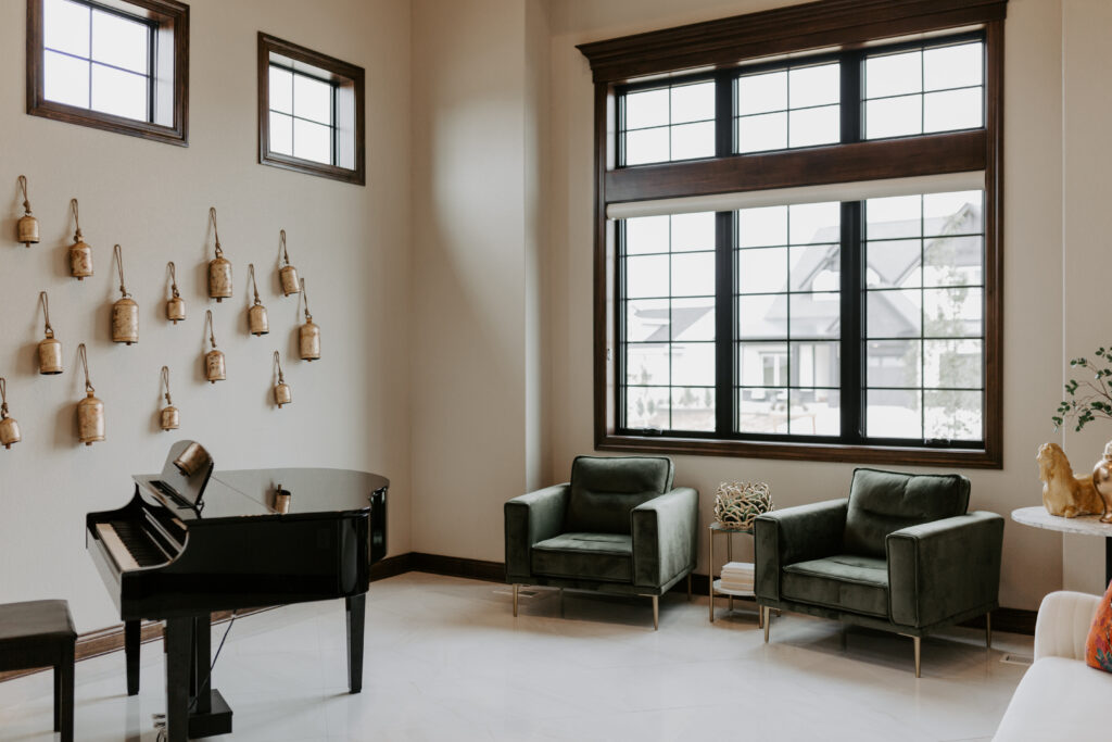 Baby grand piano with bell chimes on wall, two green velvet chairs and table in corner with gold horse statue on top. 